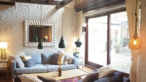 A cozy living room with a sofa, a coffee table, and a lamp. There is a window with curtains and a view of the outside.