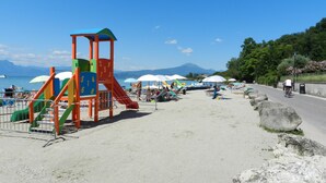 A beach with a playground, umbrellas, and a road with a cyclist.