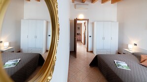 A hotel room with two beds, white wardrobes, a mirror, and a door leading to a hallway.