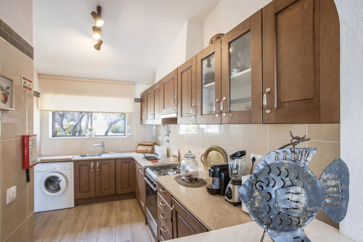 Una cocina moderna con armarios de madera, horno empotrado, lavadora y una escultura decorativa de metal.