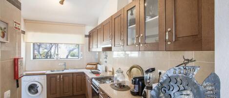 Una cocina moderna con armarios de madera, horno empotrado, lavadora y una escultura decorativa de metal.