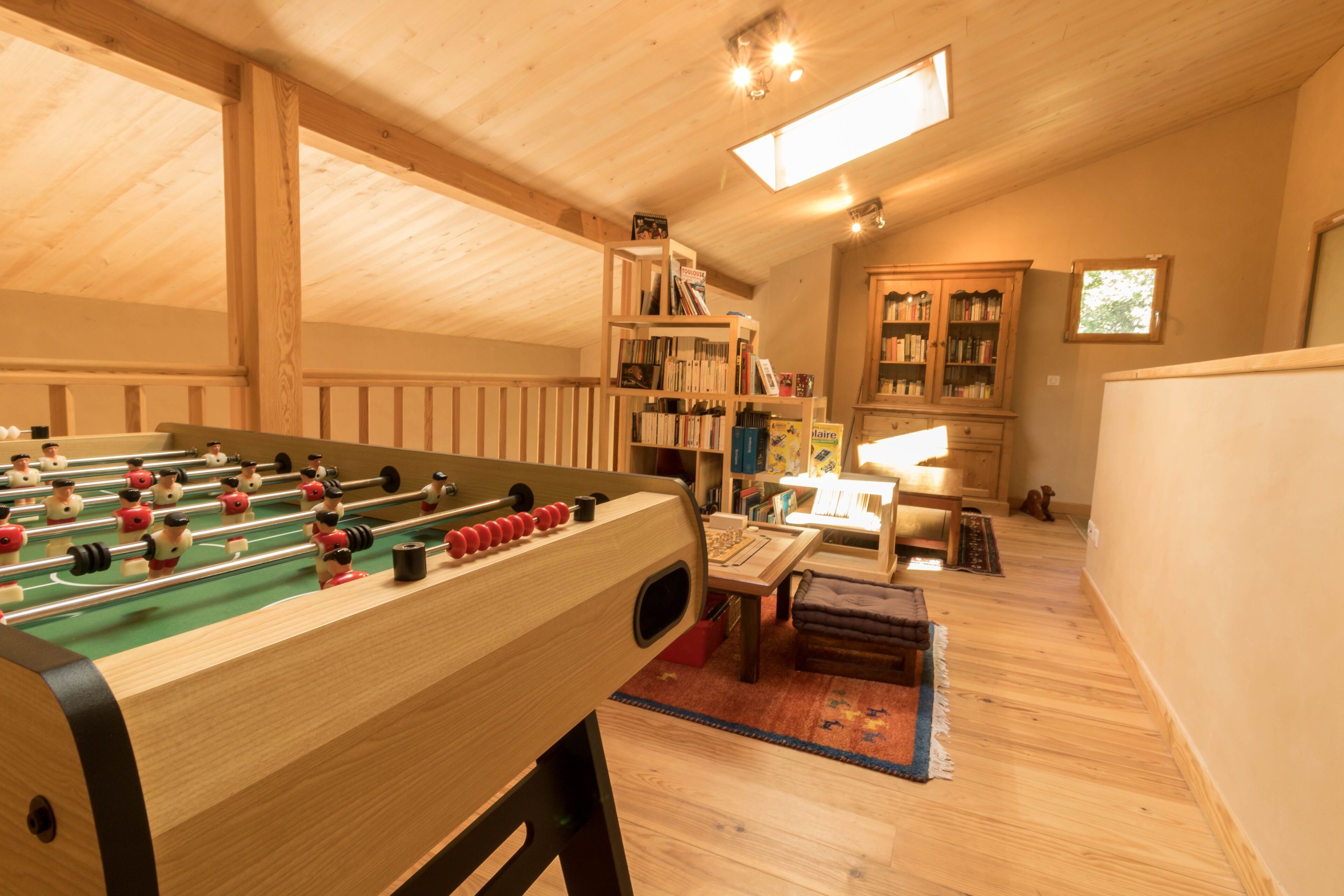 Ein gemütliches Zimmer mit einem Kicker, Bücherregalen aus Holz und einem Fenster, das für natürliches Licht sorgt.