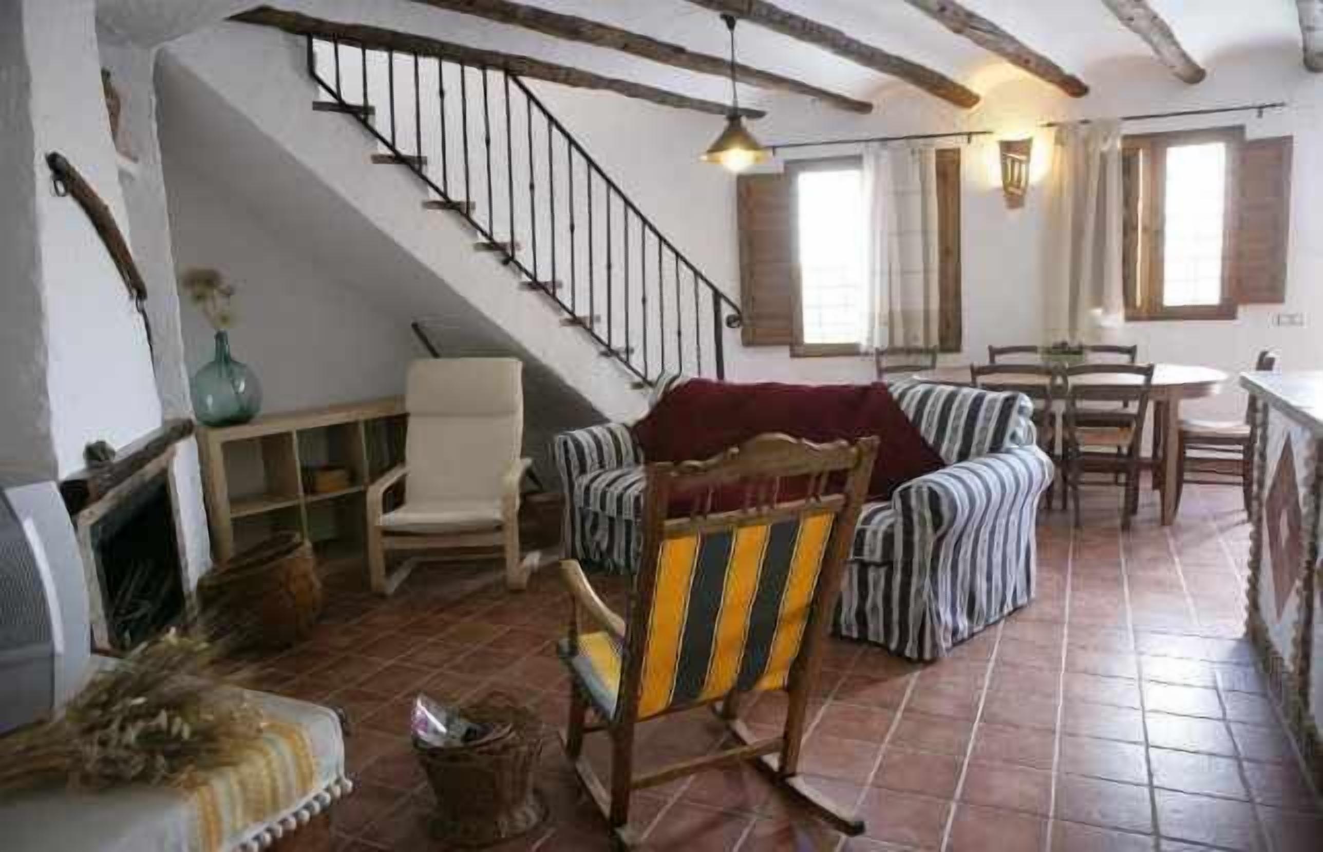 A rustic interior with a staircase, a sofa, a rocking chair, and a dining area.