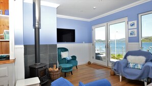 A living room with a fireplace, a television, and a view of the sea through large windows.