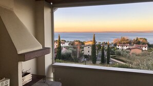 Un balcon donnant sur une ville côtière au coucher du soleil, un barbecue et une fenêtre avec vue sur la mer.