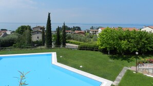 Une piscine entourée d’une pelouse, avec vue sur des maisons et la mer en arrière-plan.