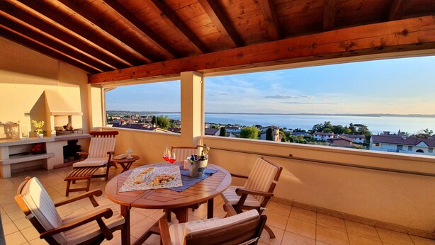 Une terrasse extérieure couverte, avec une table et des chaises en bois, un barbecue et une vue sur la mer.