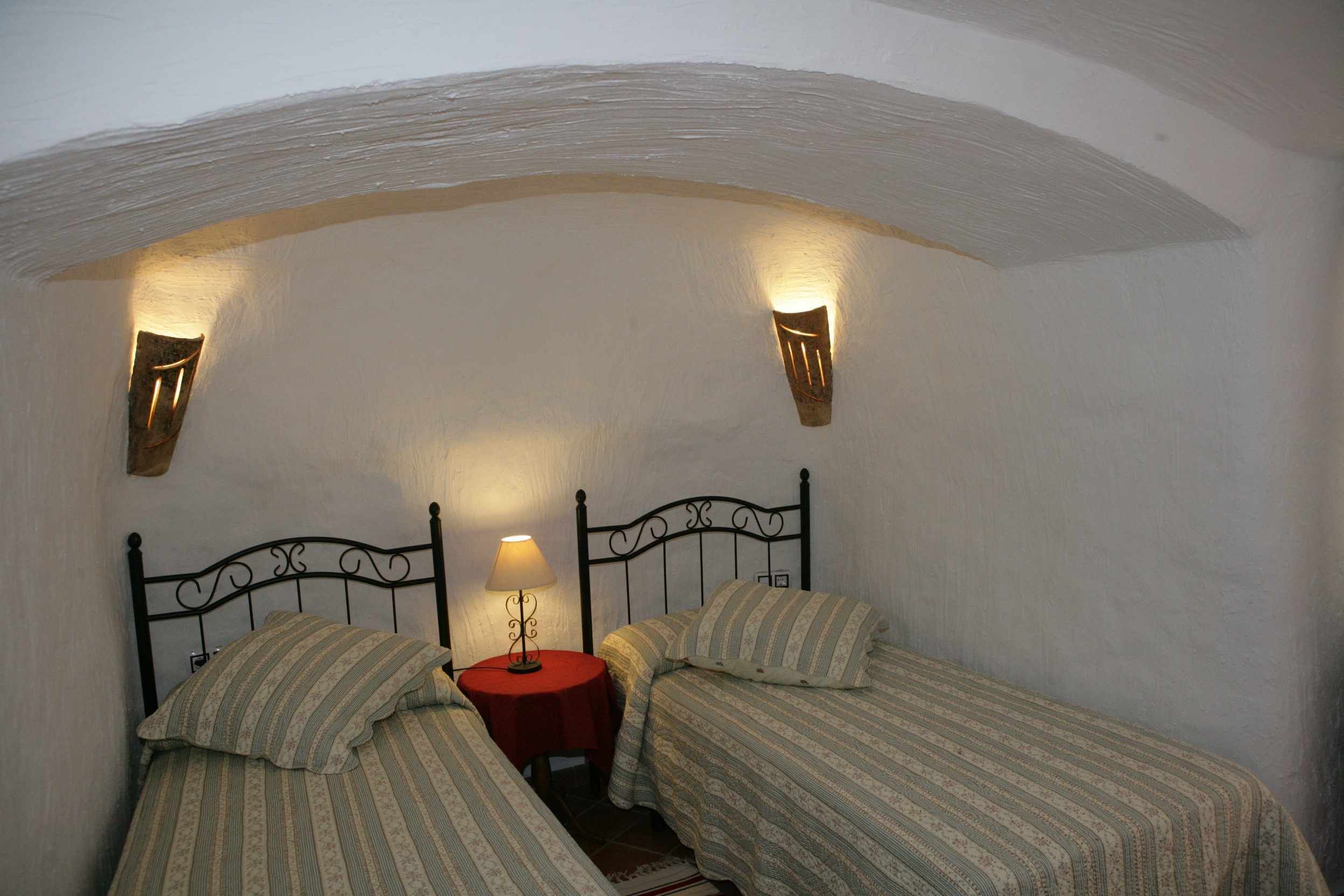 Ein kleines, gemütliches Schlafzimmer mit zwei Einzelbetten, einem roten Nachttisch und Wandleuchten.