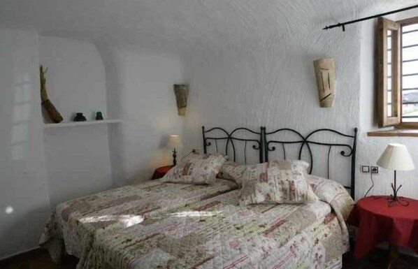 Et soveværelse med seng, natbord, lampe og et vindue.