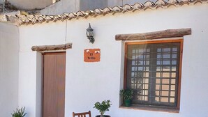 Eine Terrasse mit Tisch und vier Holzstühlen, einem Blumentopf, einem an der Wand befestigten Schild und einem Fenster mit Gittermuster.