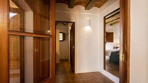 A hallway with wooden doors and a tiled floor leading to a bedroom with a bed and a nightstand. - CAN NOVES - Detached, central and peaceful villa (Sant Francesc de Formentera)