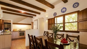A kitchen with wooden beams, a dining table with chairs, and a window with a view of greenery. - CAN NOVES - Detached, central and peaceful villa (Sant Francesc de Formentera)