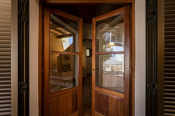 A wooden double door with glass panels, leading into a hallway with a tiled floor.