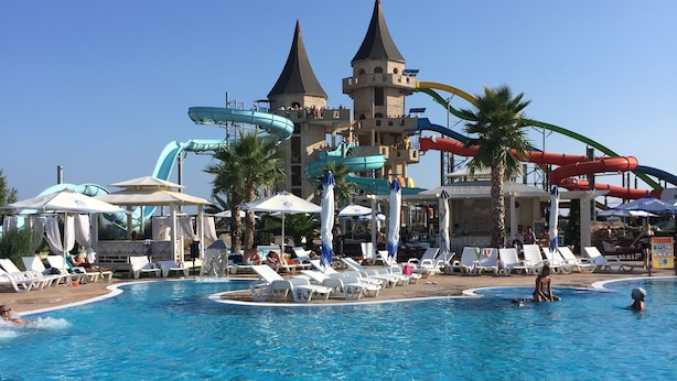 Una piscina con toboganes de agua y sombrillas, rodeada de tumbonas y palmeras.