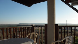 Un espacio exterior cubierto con una mesa y dos sillas, con vistas a un paisaje de colinas distantes.