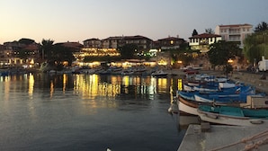 Una zona frente al agua con barcos amarrados, edificios con letreros iluminados y un agua tranquila que refleja las luces.