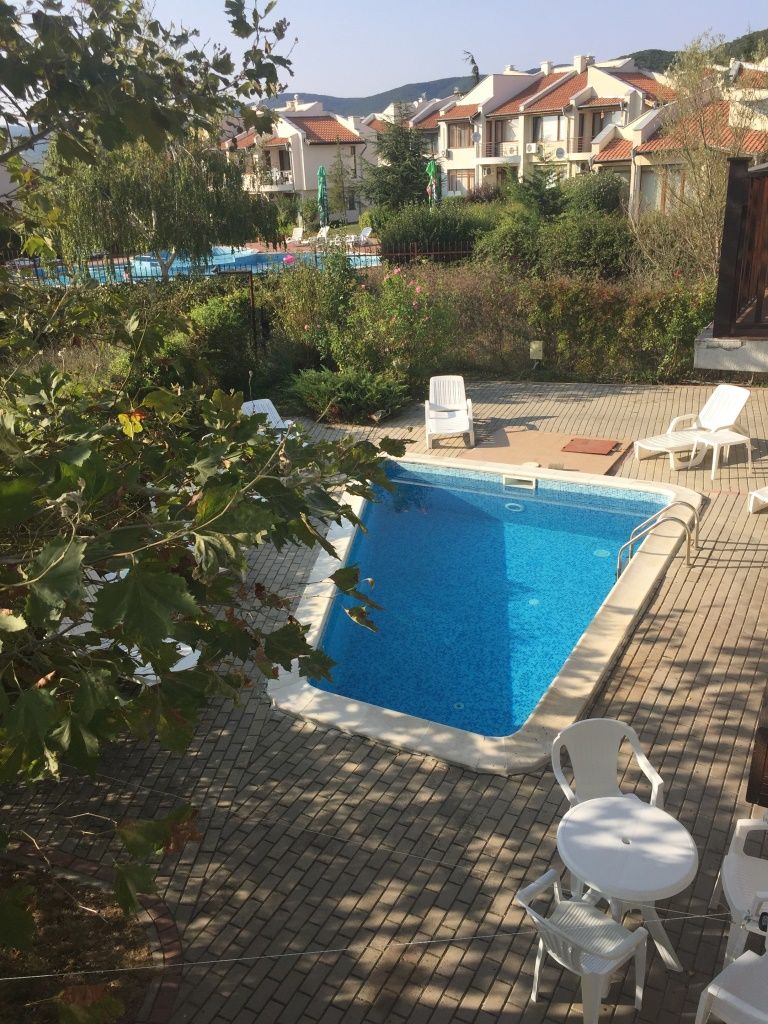 Ein Swimmingpool mit Liegestühlen und einem Tisch, umgeben von Grünflächen und Gebäuden im Hintergrund.