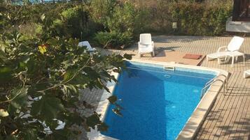 Ein Swimmingpool mit Liegestühlen und einem Tisch, umgeben von Grünflächen und Gebäuden im Hintergrund.