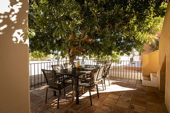 Eine Terrasse im Freien mit Tisch und Stühlen, umgeben von einem gefliesten Boden und einem Metallgeländer.