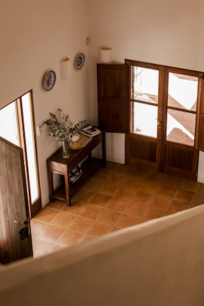 Une pièce d’angle avec un bureau en bois, un vase de fleurs et une vue sur l’extérieur, visible à travers une porte.