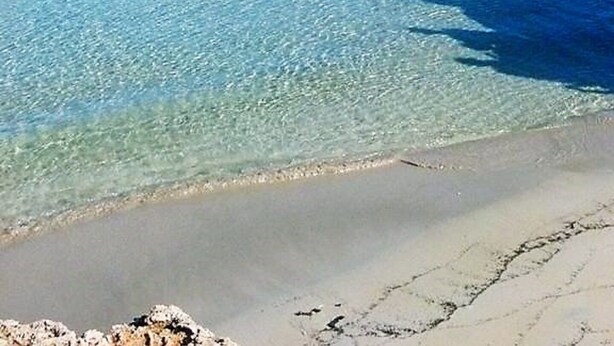 Ein Strand mit klarem Wasser, einem Felsen und einem Sandufer.