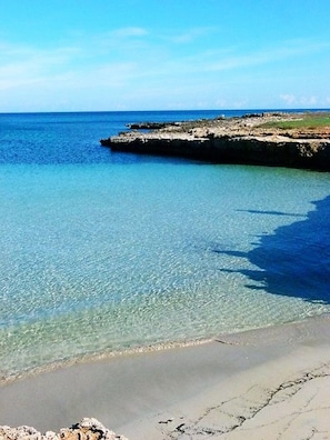 Una playa con agua cristalina, un promontorio rocoso y una orilla arenosa.