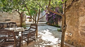 Eine Terrassengruppe im Freien mit Korbmöbeln, einer Steinmauer und einem Baum mit violetten Blüten.
