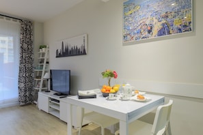 Ein modernes Wohnzimmer mit einem weißen Tisch, gedeckt für das Frühstück, einem Fernseher und einem Stadtbild an der Wand.