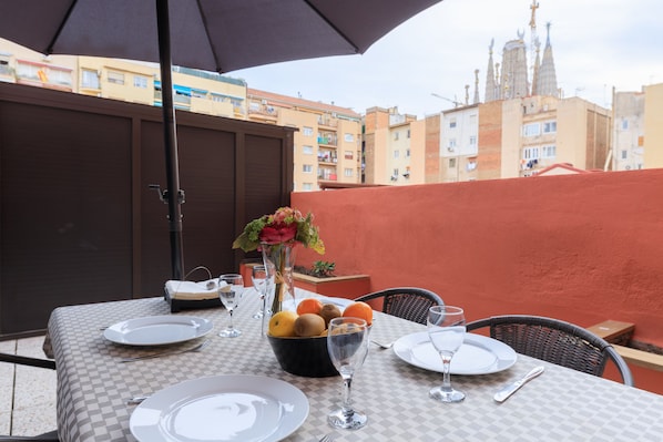 Ein Esstisch mit Geschirr, Besteck und Obstschale, mit Blick auf eine Stadtlandschaft und markanter Architektur.