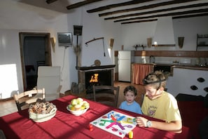 Un comedor con una mesa dispuesta para dos personas, una chimenea y una cocina al fondo.