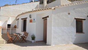 A white building with a tiled roof, a wooden table and chairs, a potted plant, and a sign indicating a restaurant.
