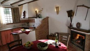A rustic kitchen with a brick wall, a fireplace, and a dining table set with a red tablecloth and a bottle of wine.