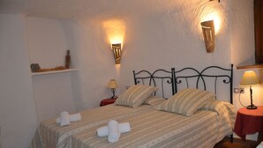 A bedroom with a bed, two wall-mounted lamps, a nightstand, and a shelf with a bottle and a small object.