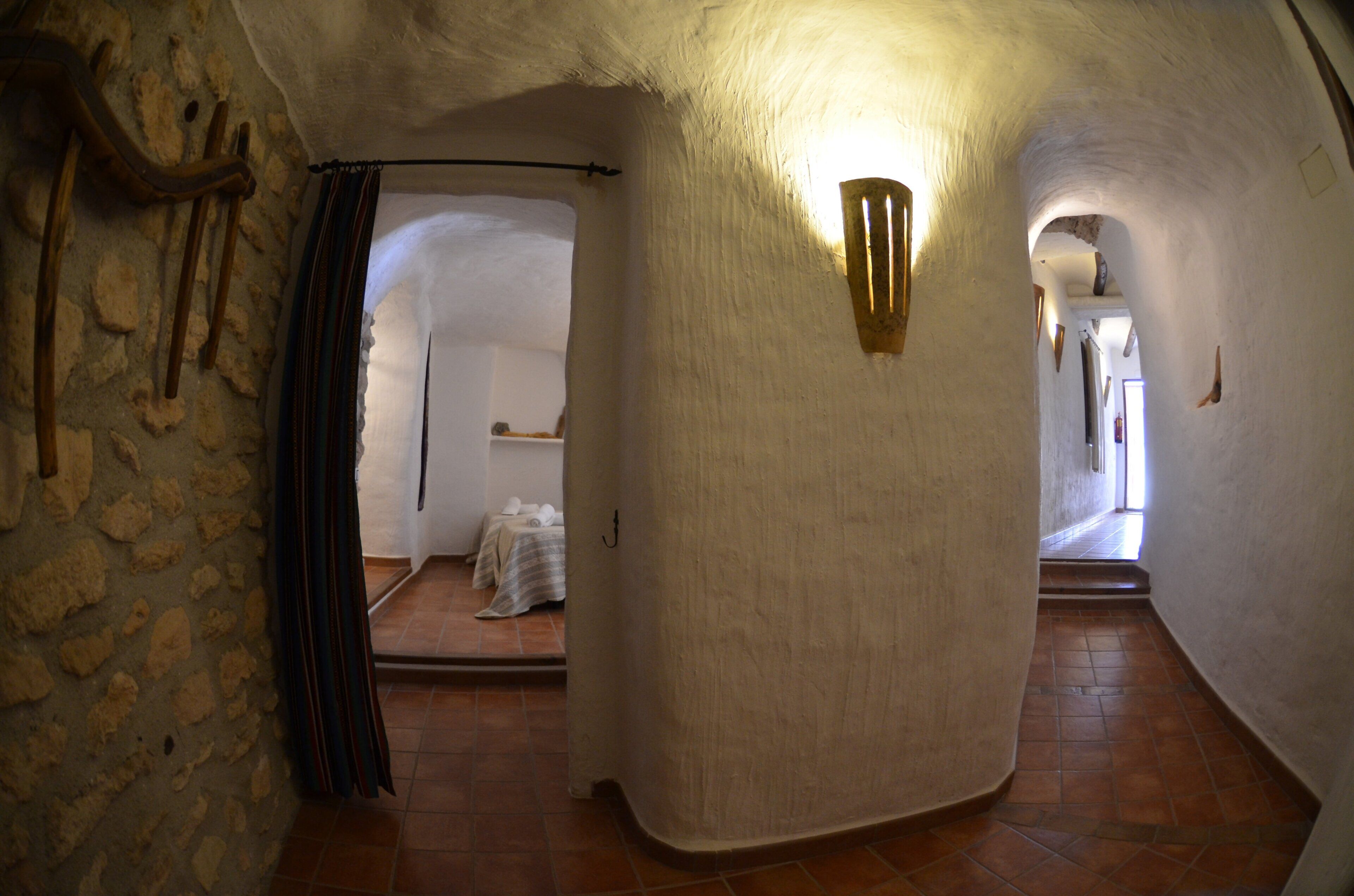 Un couloir étroit aux murs de pierre, doté d’un sol carrelé, et un lit visible au fond.