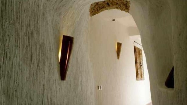 A narrow, arched hallway with rough, textured walls and minimal lighting fixtures.