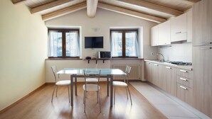 Una cocina moderna con vigas de madera, un comedor con mesa y sillas de vidrio, y vistas a montañas a través de las ventanas.