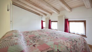 Un dormitorio con cama, vigas de madera en el techo, una ventana con cortinas y un radiador.