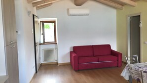 Una habitación con techo de madera, un sofá rojo, un radiador, una ventana y una mesa con sillas.
