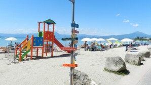 Une plage dotée d’une aire de jeux pour enfants, de parasols et d’un panneau indicateur.