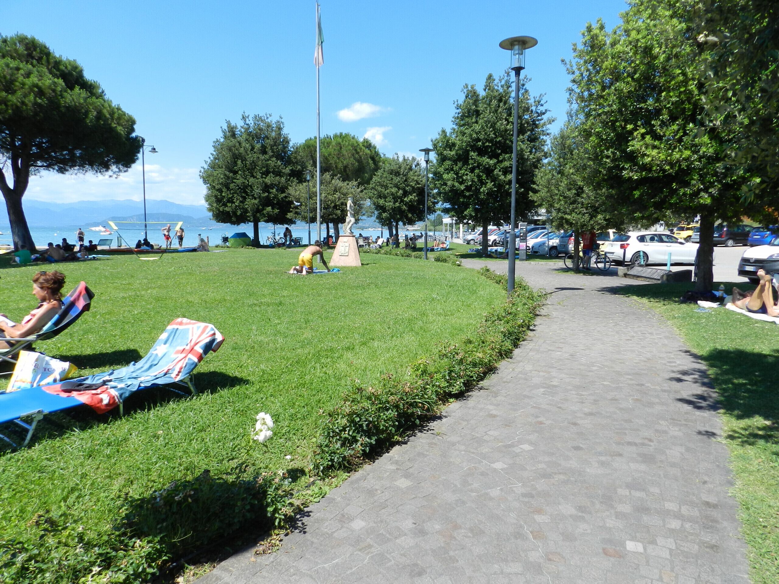 A park with grass, trees, a statue, and a paved path.