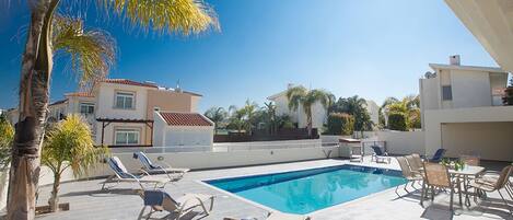A swimming pool with lounge chairs and a table, surrounded by palm trees and buildings.
