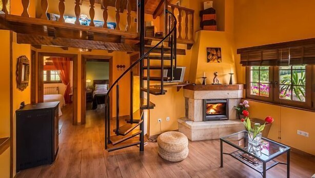 A spacious living area with a wooden staircase, a fireplace, and a large window with a view of greenery. - Rural house (full rental) "Casucas La Guariza" for 6 people (Hermandad de Campoo de Suso)