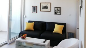 Una sala de estar moderna con un sofá negro, cojines amarillos, una mesa de centro de vidrio, un sillón blanco y obras de arte enmarcadas en la pared.