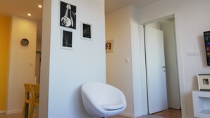 Una sala de estar moderna con una silla blanca, un comedor con sillas amarillas y obras de arte en las paredes.