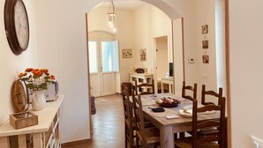 A dining area with a wooden table and chairs, a clock on the wall, and a vase with flowers on a side table. - Dimora del Vico - Suite Elite (Lecce)