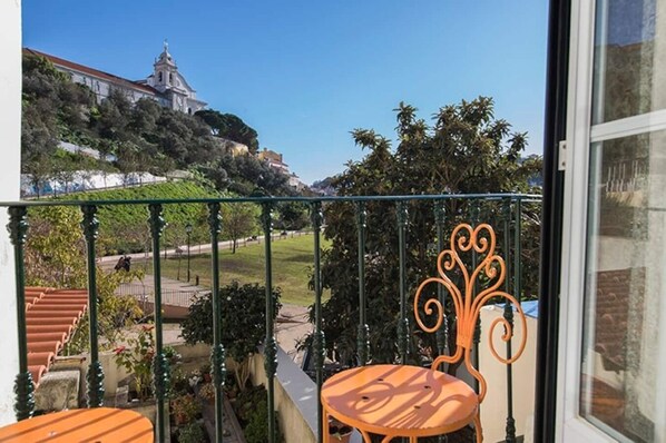 A balcony with a view of a hilltop building, a garden, and a street.