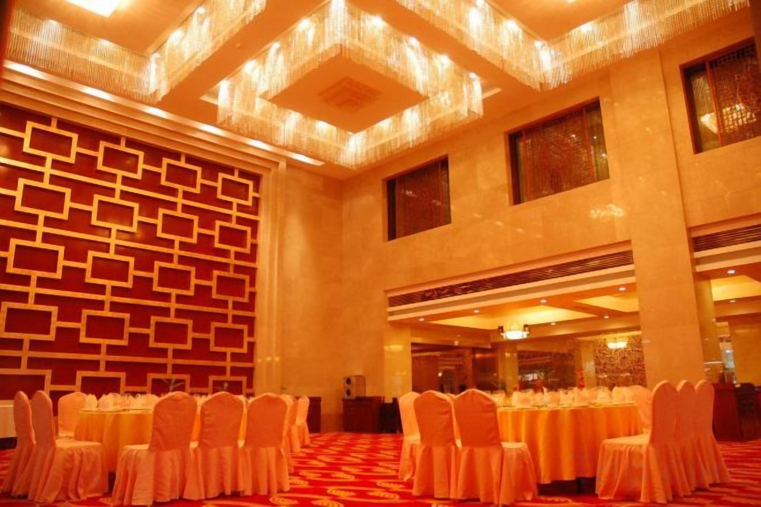 A banquet hall with rows of round tables, chairs, and a patterned wall.