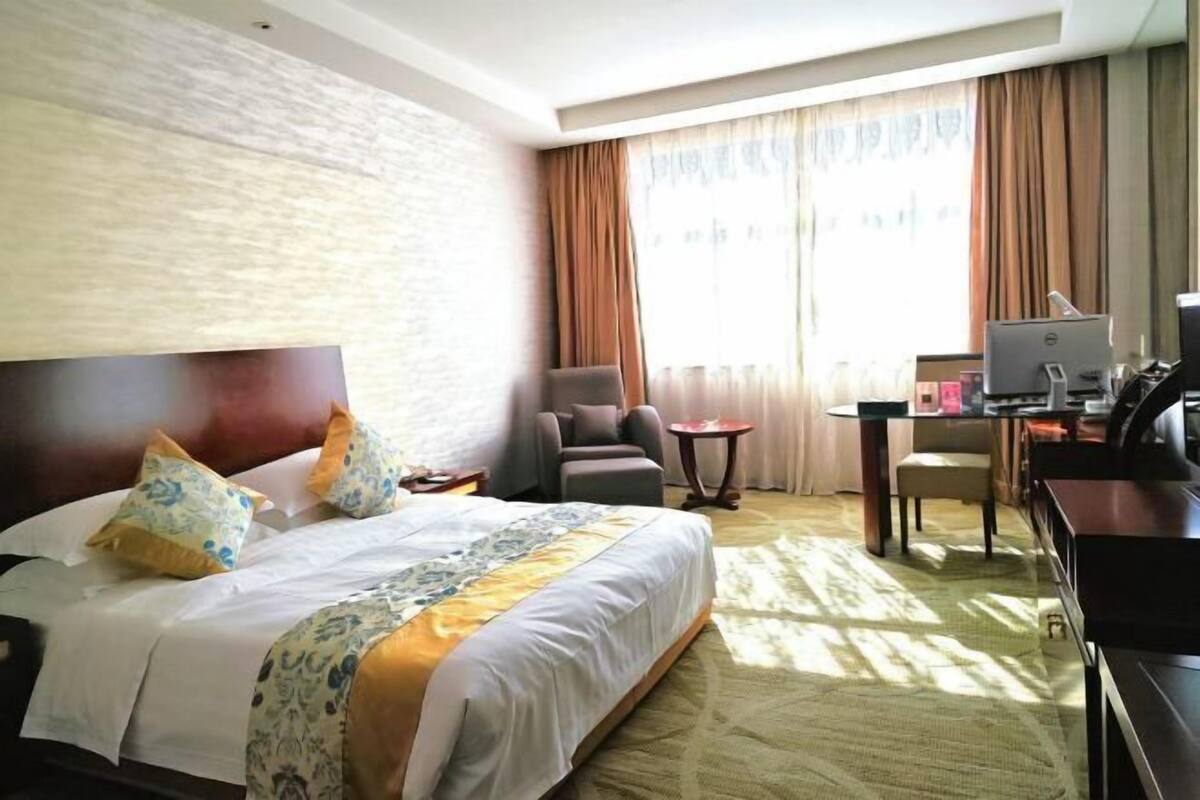A hotel room with a large bed, a desk with a computer, a chair, and a small table.