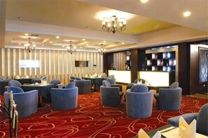 A hotel lobby with round tables, blue chairs, a reception desk, and a chandelier.