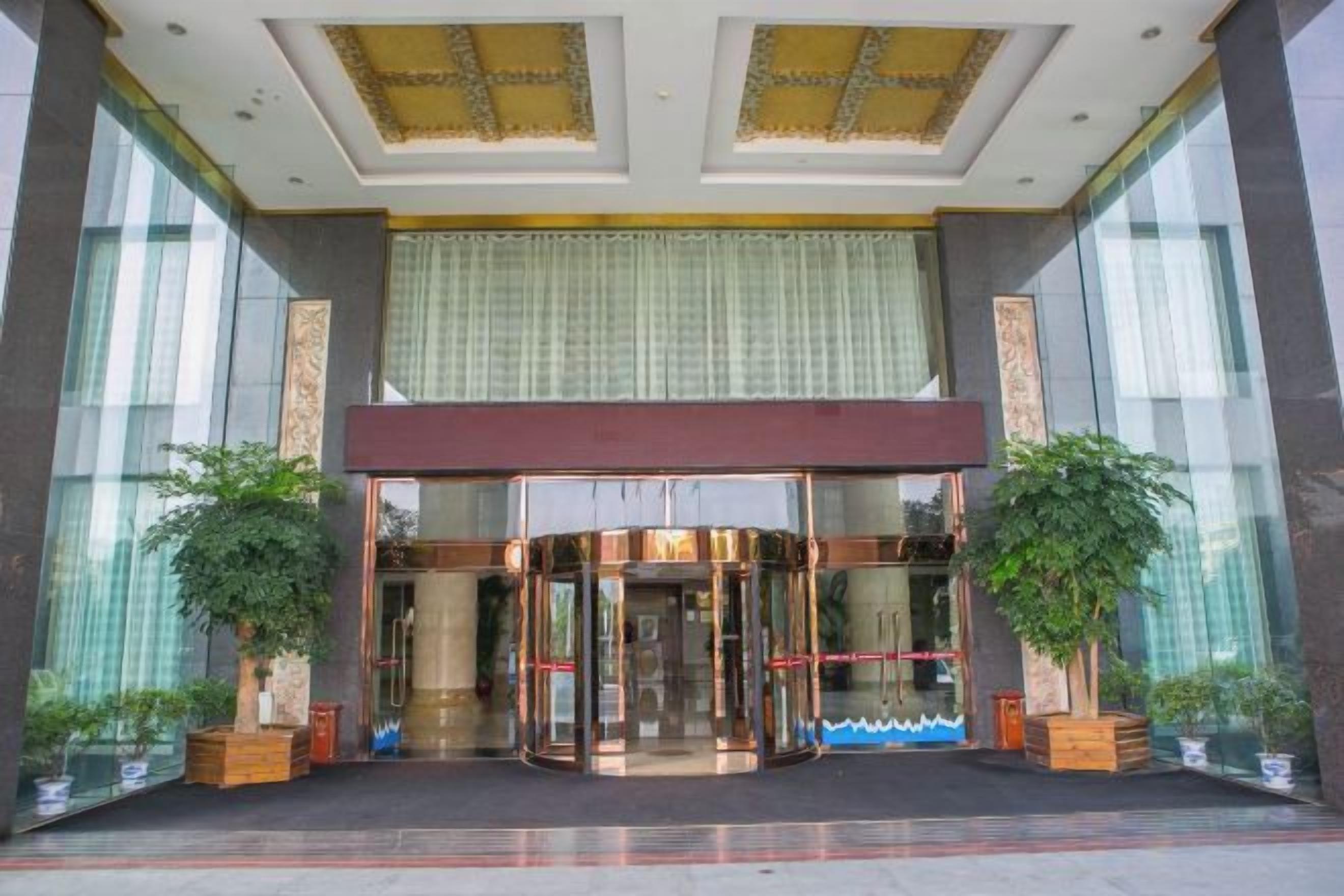 Entrada de hotel con puerta giratoria, ventanas amplias y plantas en macetas.
